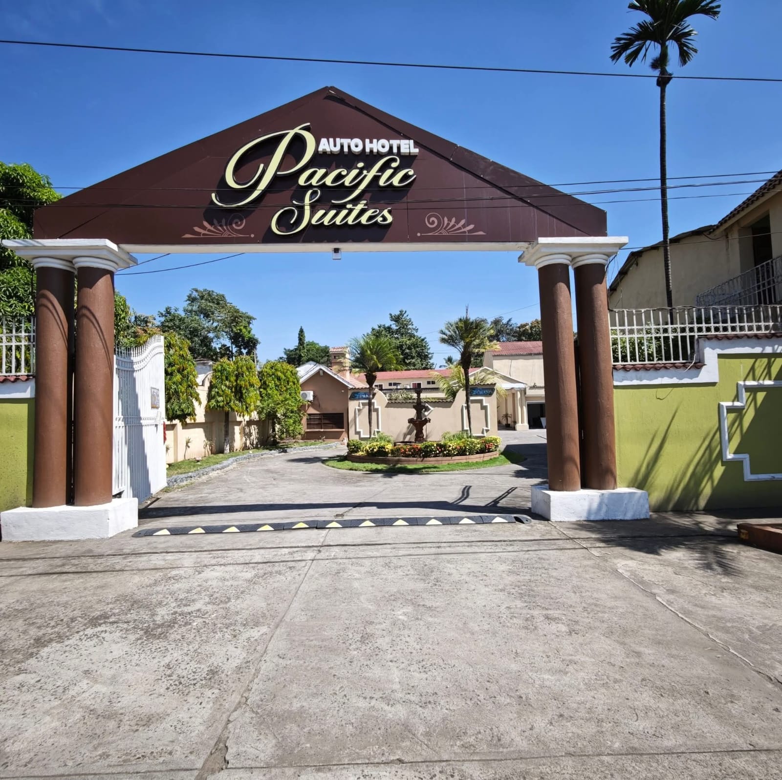 Fachada actual de Pacific Suites Autohotel, con su rótulo dorado, columnas y jardines