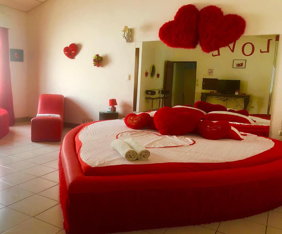 Love, habitación 20: cama roja y blanca con cojines de corazón y espejo